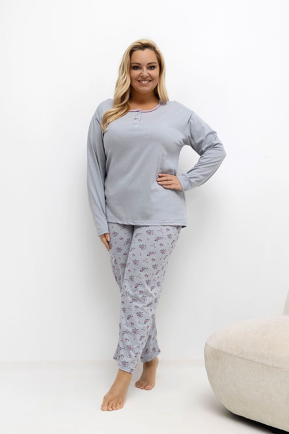 Woman wearing a light gray pajama set with floral pants on a white background