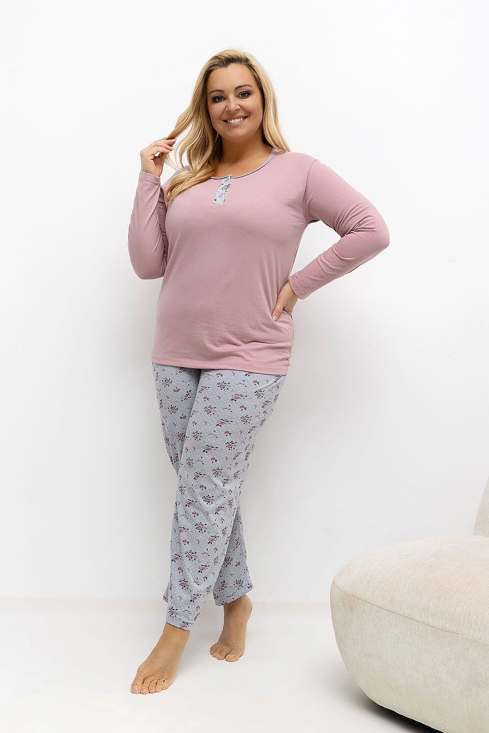 Woman wearing a pink long-sleeve top and gray floral pants on a white background