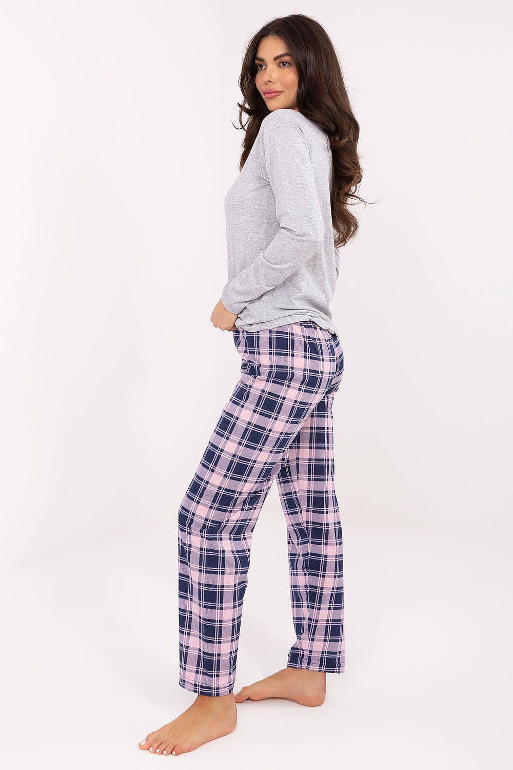 Woman wearing a gray long-sleeve top and plaid pants on a white background