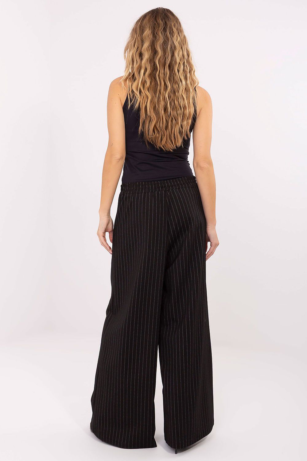 Person wearing black pleated pants on a white background