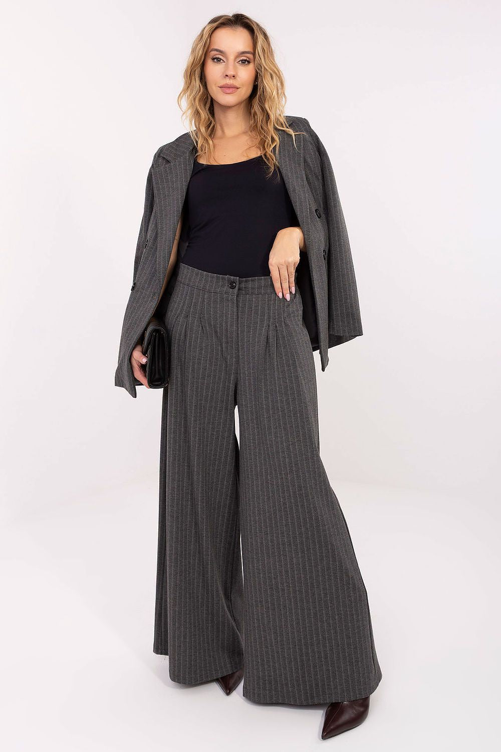 Woman wearing a black top and gray pinstripe pants with a matching jacket on a white background