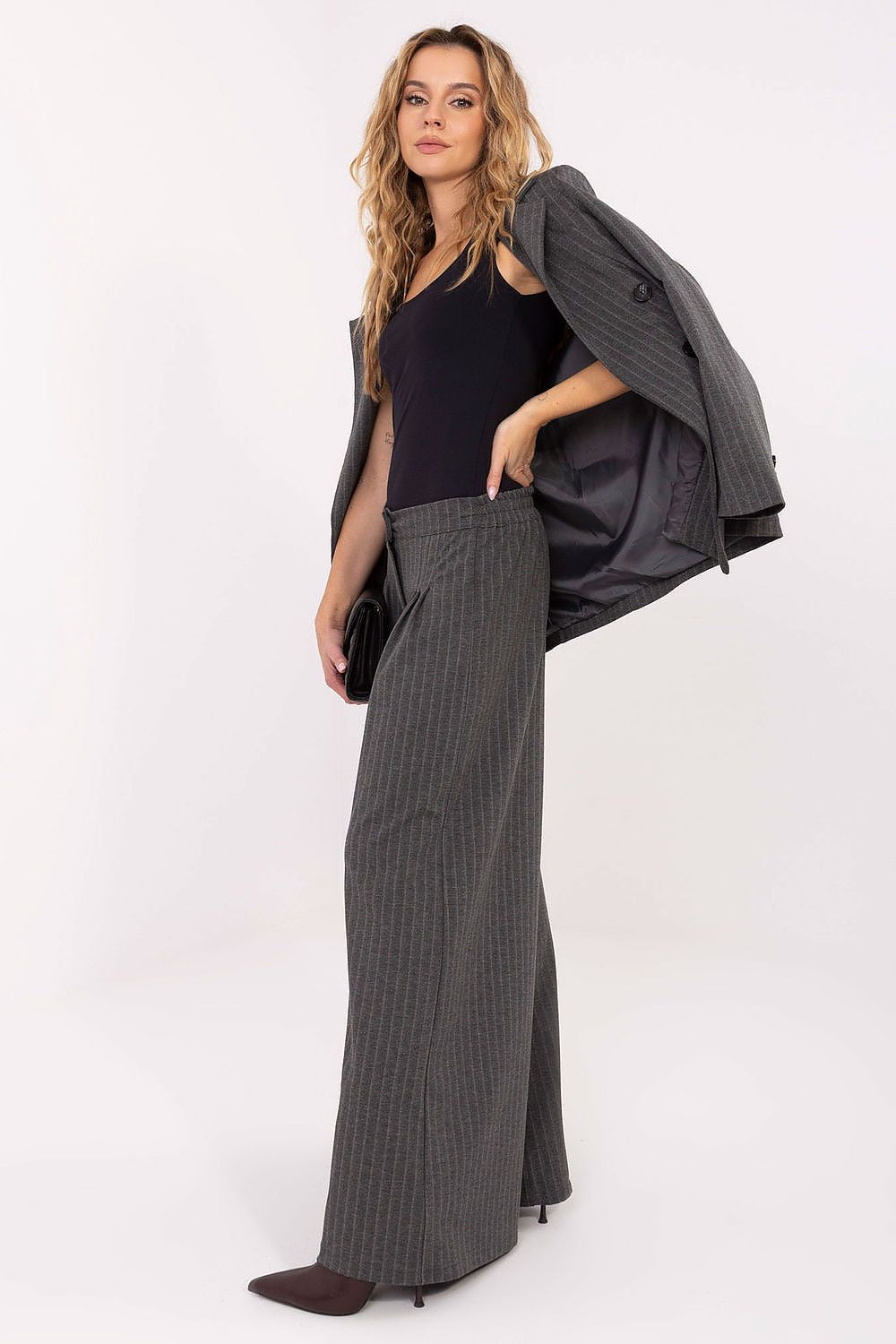 Woman wearing a black top, gray pinstripe pants, and a gray jacket on a white background