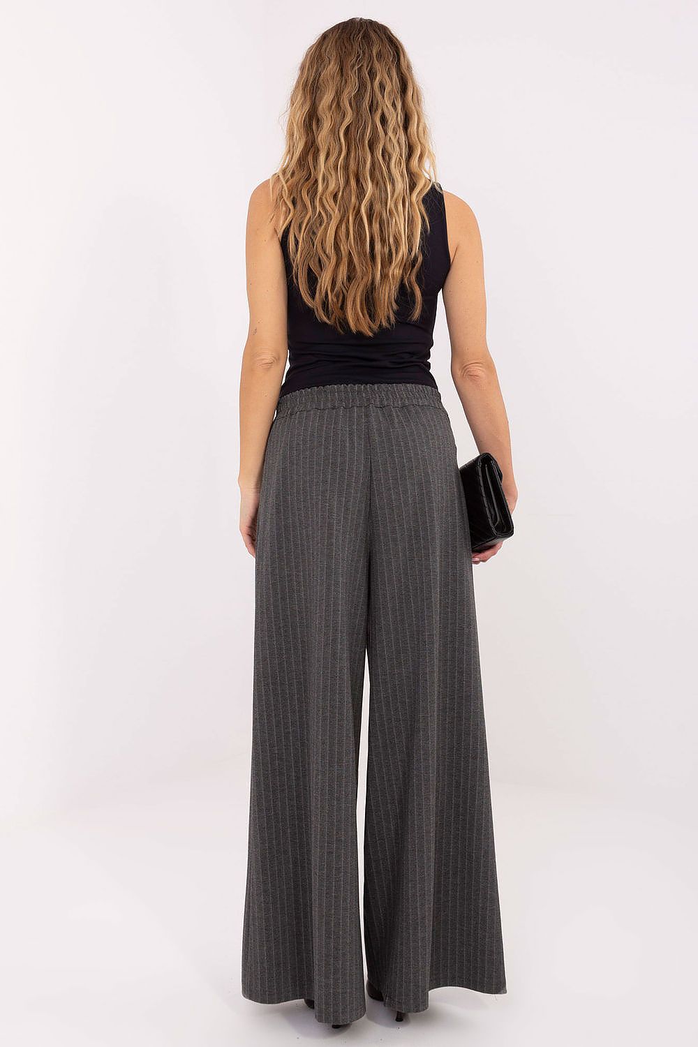 Woman wearing a black sleeveless top and gray wide-leg pants on a white background