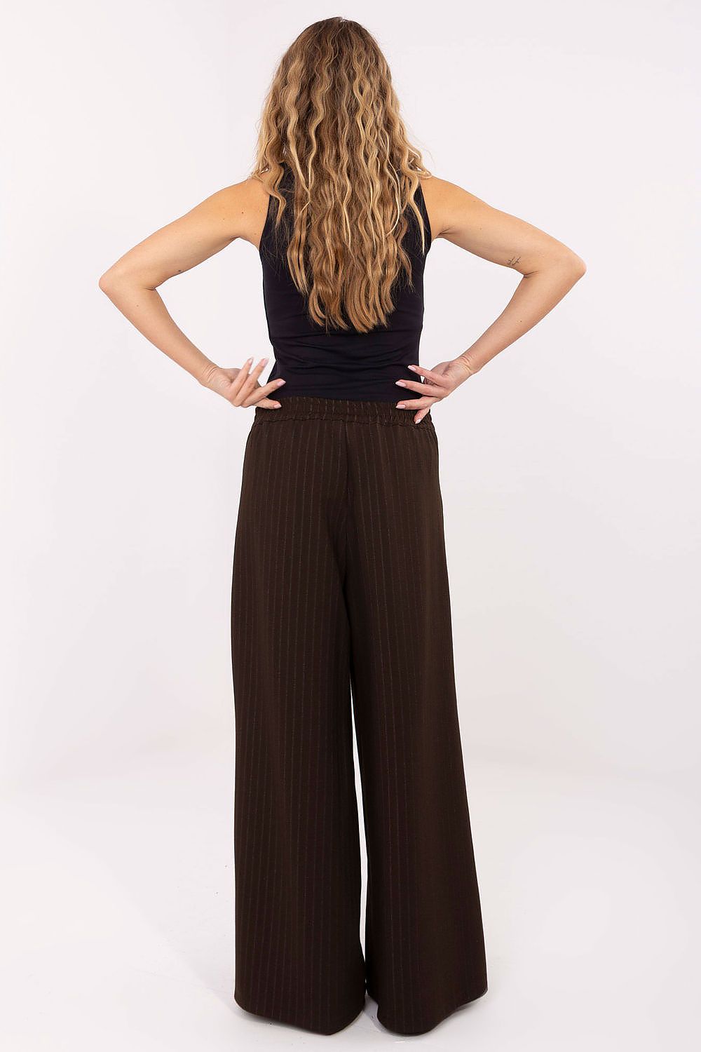 Woman wearing brown ribbed wide-leg pants and a black sleeveless top on a white background