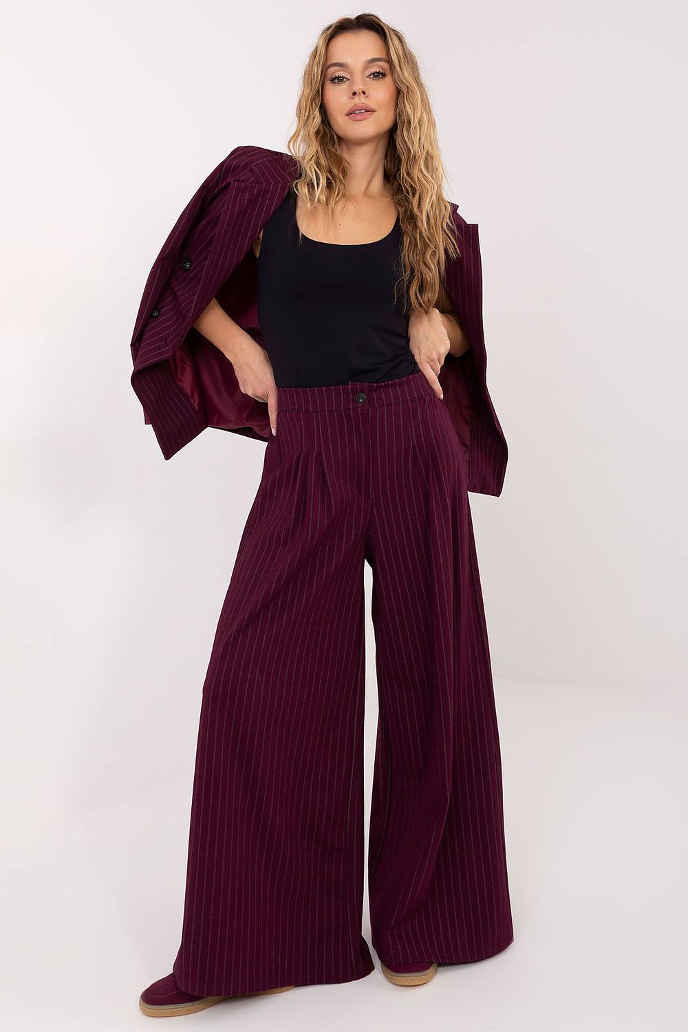 Woman wearing a burgundy outfit with wide-leg pants and a matching jacket on a white background