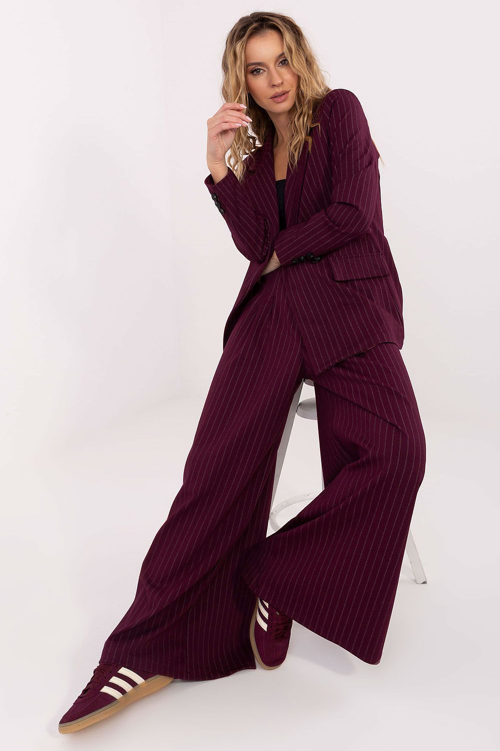 Woman wearing a ribbed purple outfit sitting on a white stool against a white background