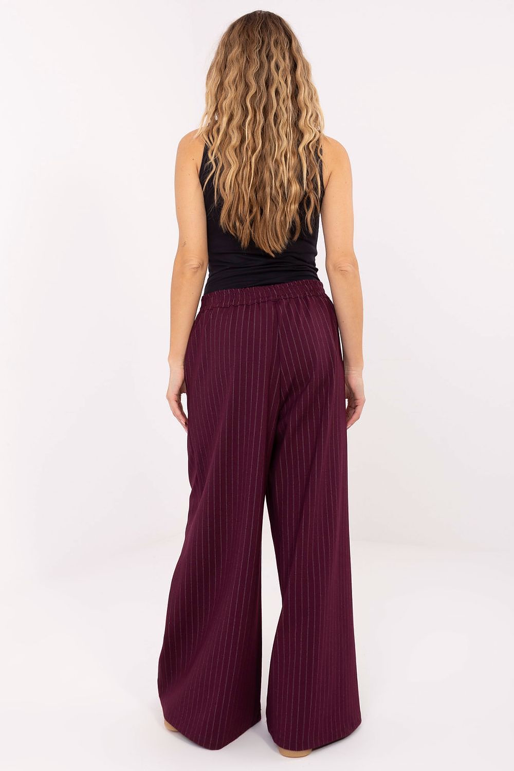 Woman wearing burgundy wide-leg pants and a black top on a white background