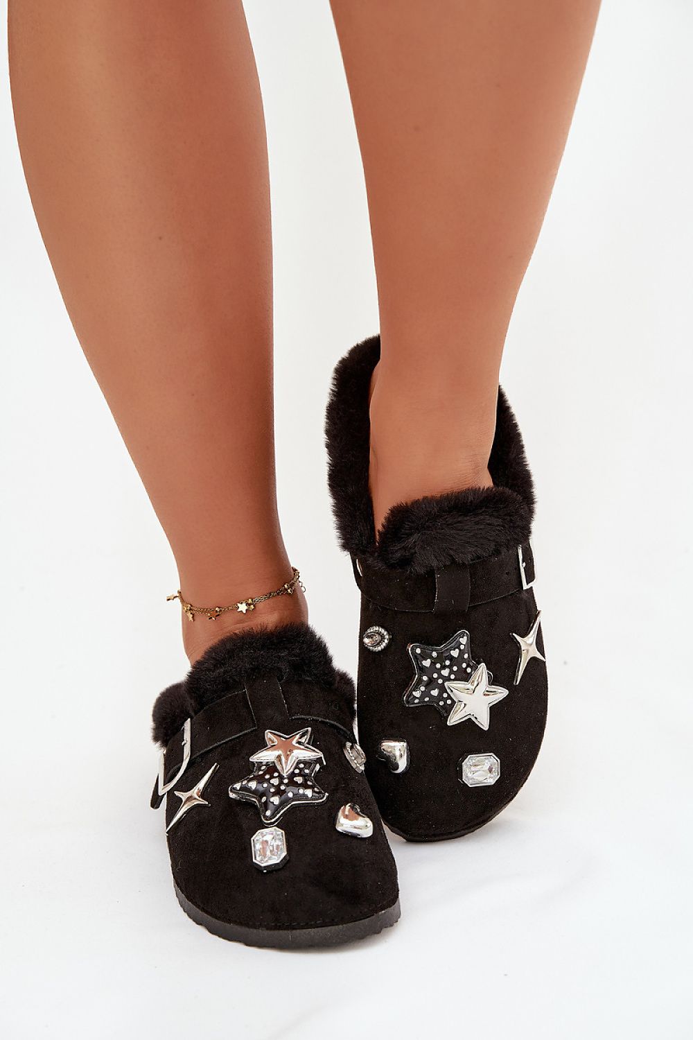 Black slippers with star designs and fur trim worn by a person on a white background