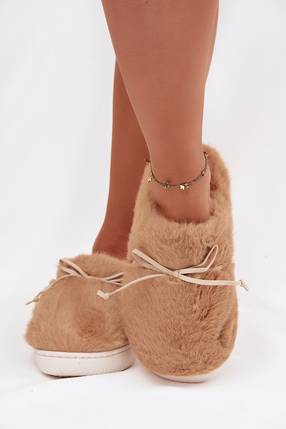 Tan fuzzy slippers worn by a person on a white background