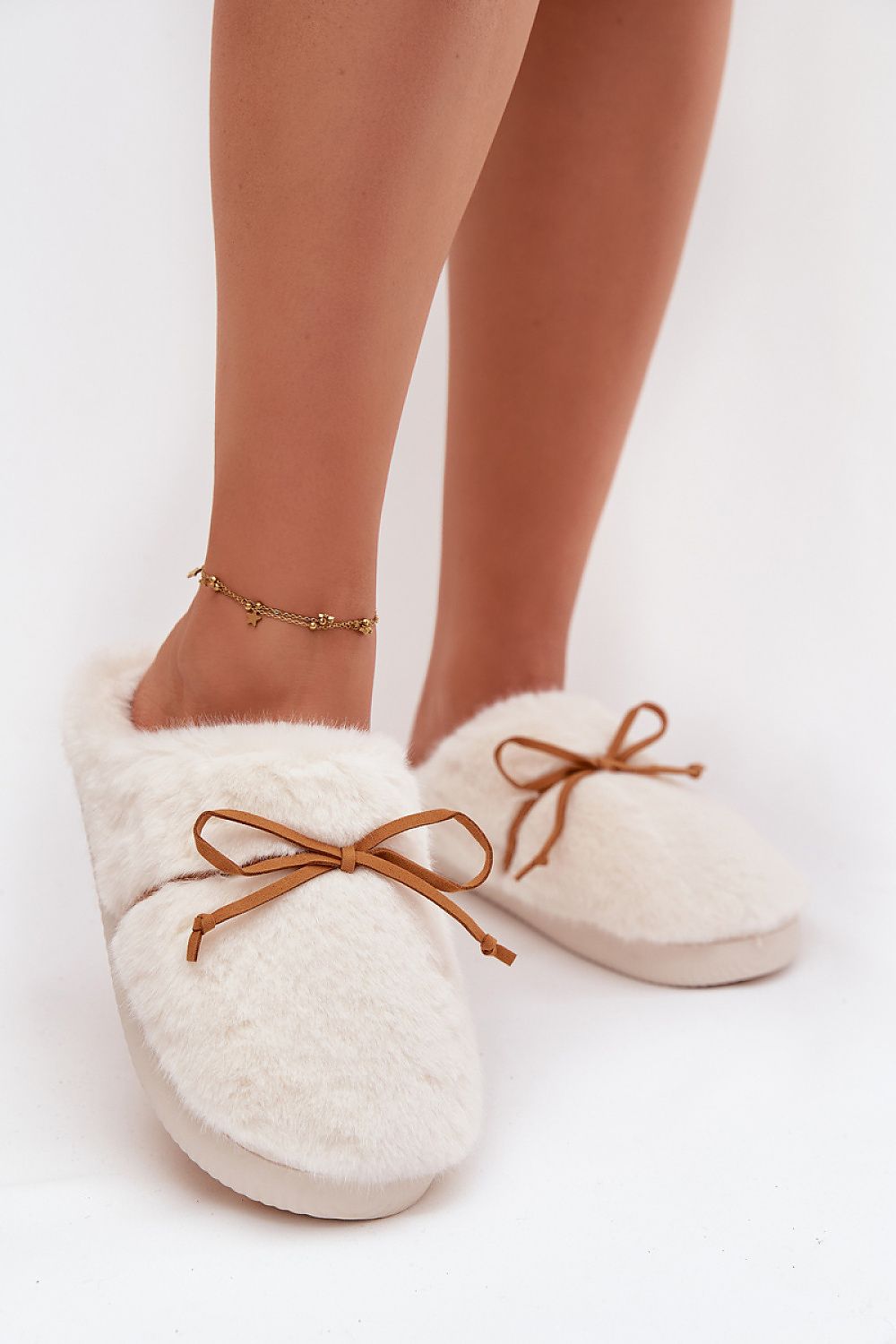 White fuzzy slippers with brown laces worn by a person on a white background