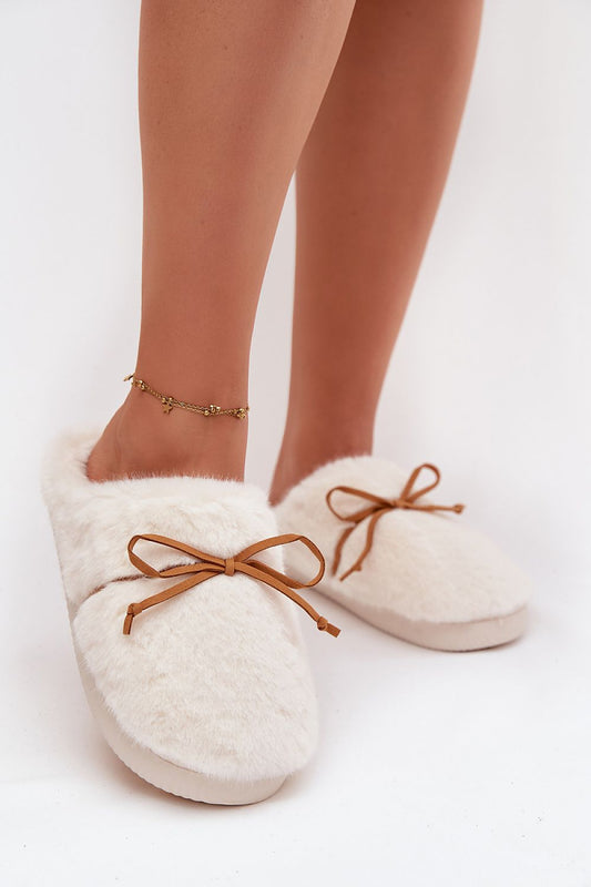 White fuzzy slippers with brown laces worn by a person on a white background