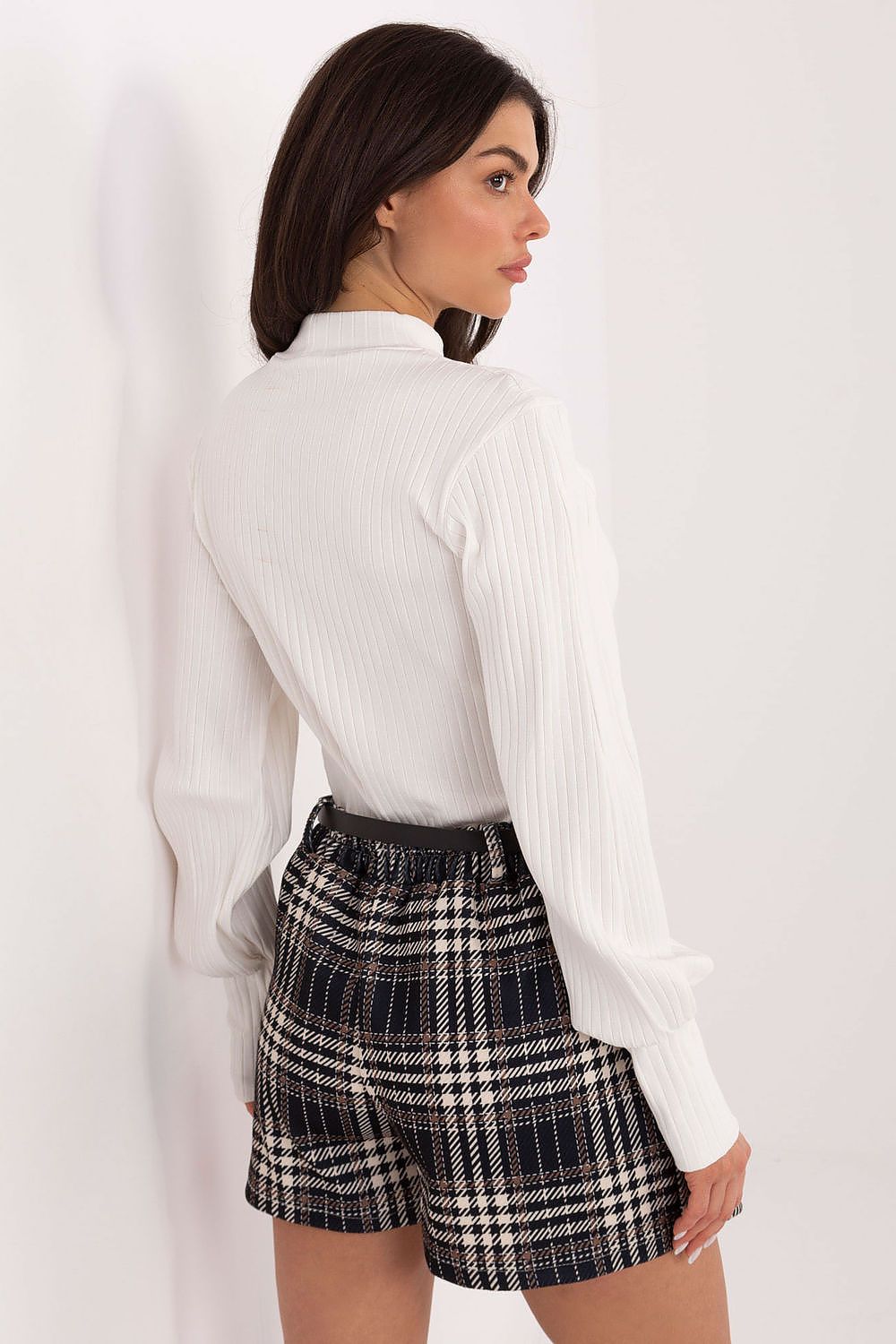 Woman wearing a white blouse and plaid shorts against a white background