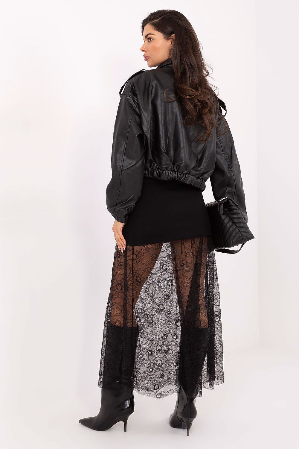 Woman wearing a black jacket and a long, patterned dress on a white background