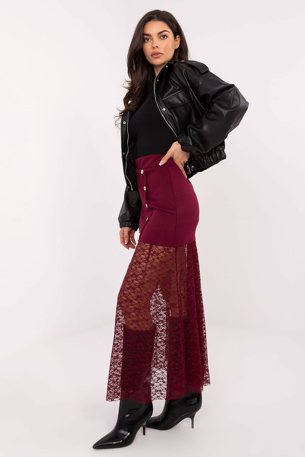Woman wearing a black leather jacket, black top, and burgundy skirt with lace overlay on a white background