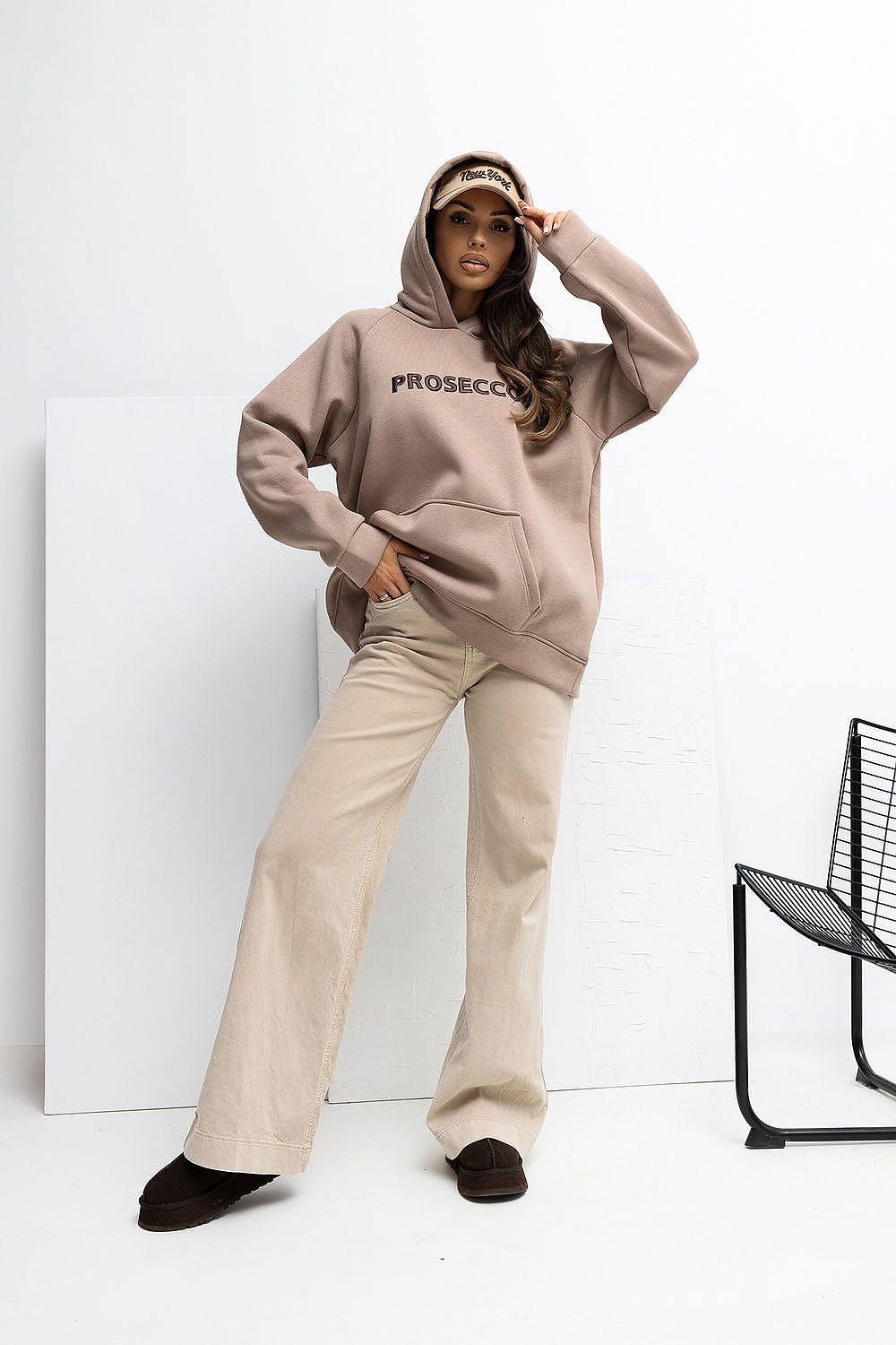 Person wearing a beige hoodie with 'PROSECCO' text and beige pants against a white background.
