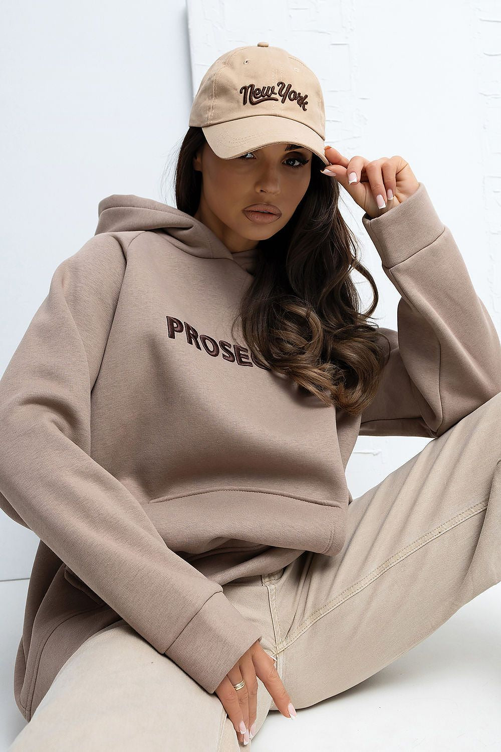 Woman wearing a beige hoodie and pants with a matching cap, sitting on a white floor.