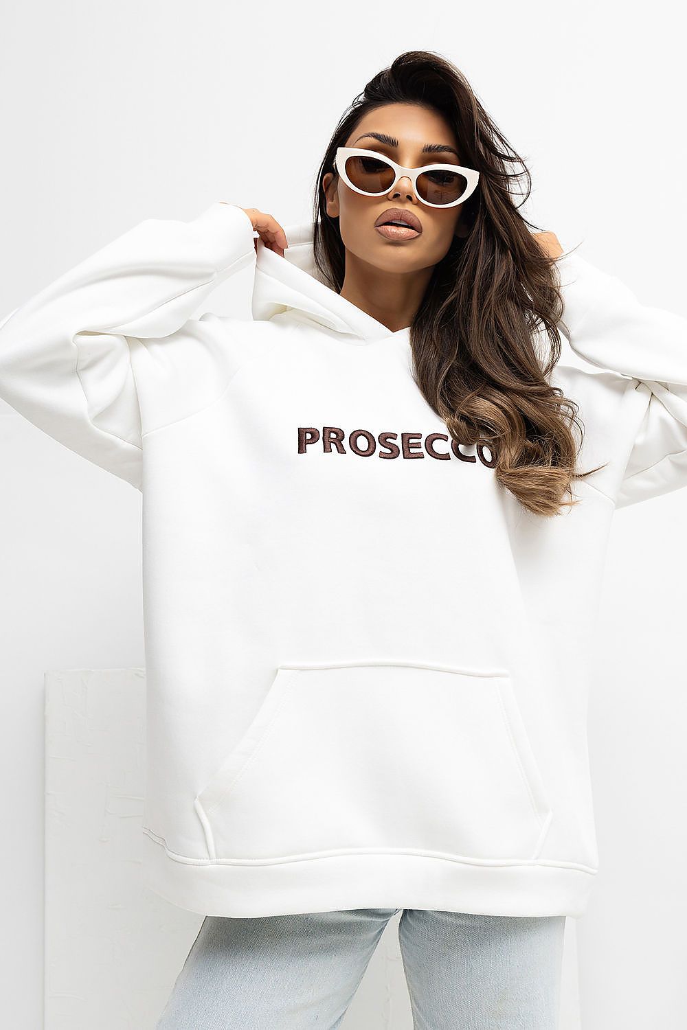 Woman wearing a white hoodie with 'PROSECCO' text and light blue pants on a white background