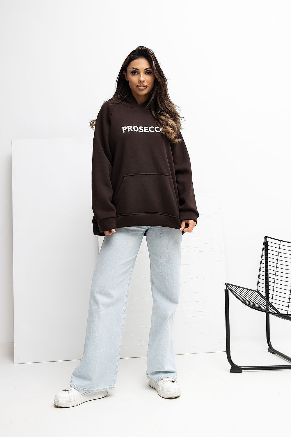 Woman wearing a brown hoodie with 'PROSECCO' text, standing against a white background.