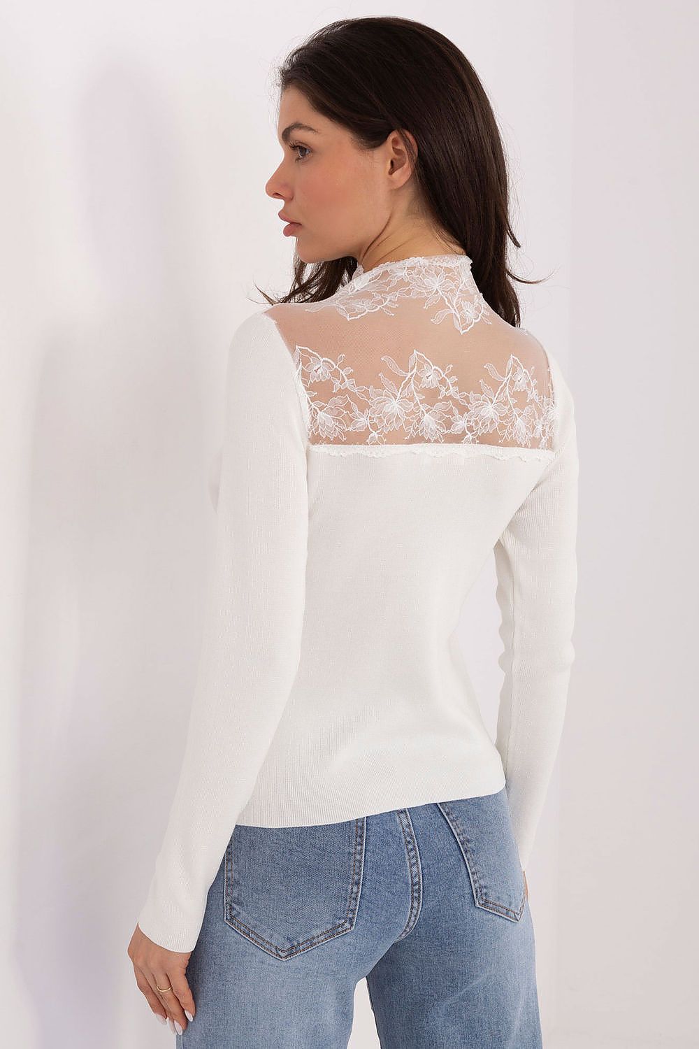 Woman wearing a white blouse with lace detailing and blue jeans on a white background