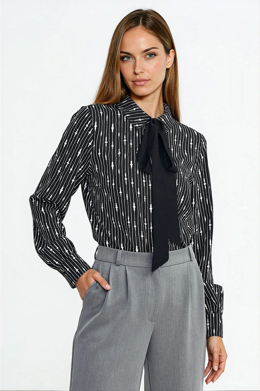 Woman wearing a black and white patterned blouse with a black tie and gray pants on a white background