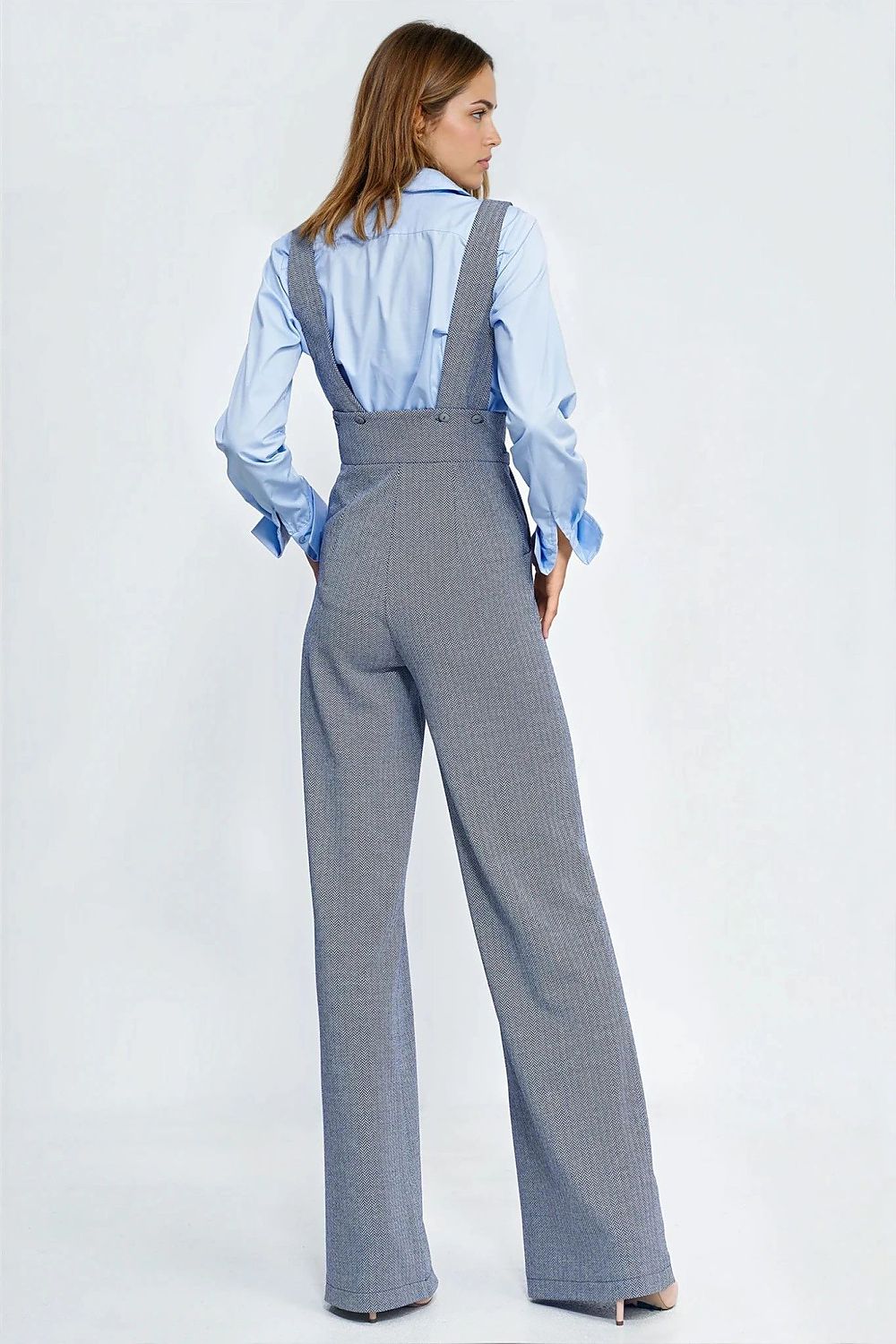 Woman wearing a gray checkered jumpsuit with a blue shirt underneath on a white background