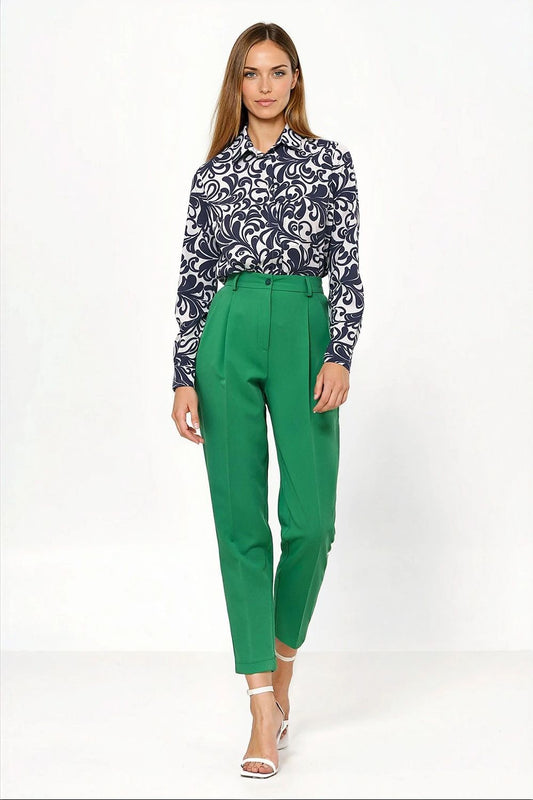 Woman wearing a patterned blouse and green pants on a white background