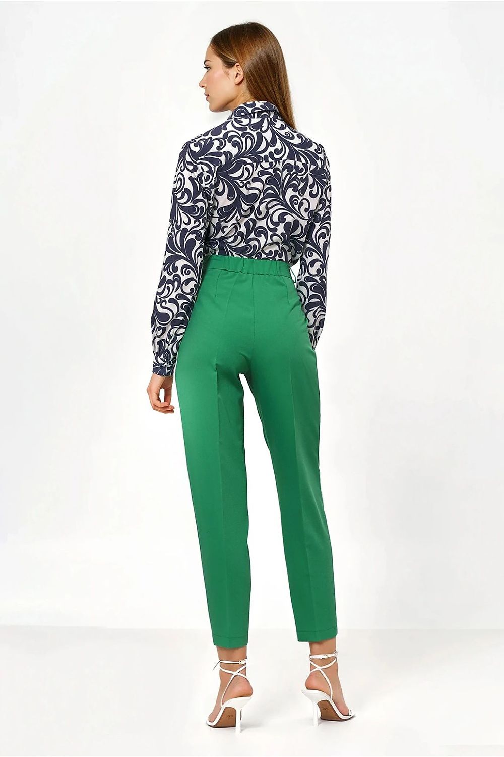 Woman wearing a patterned blouse and green pants on a white background