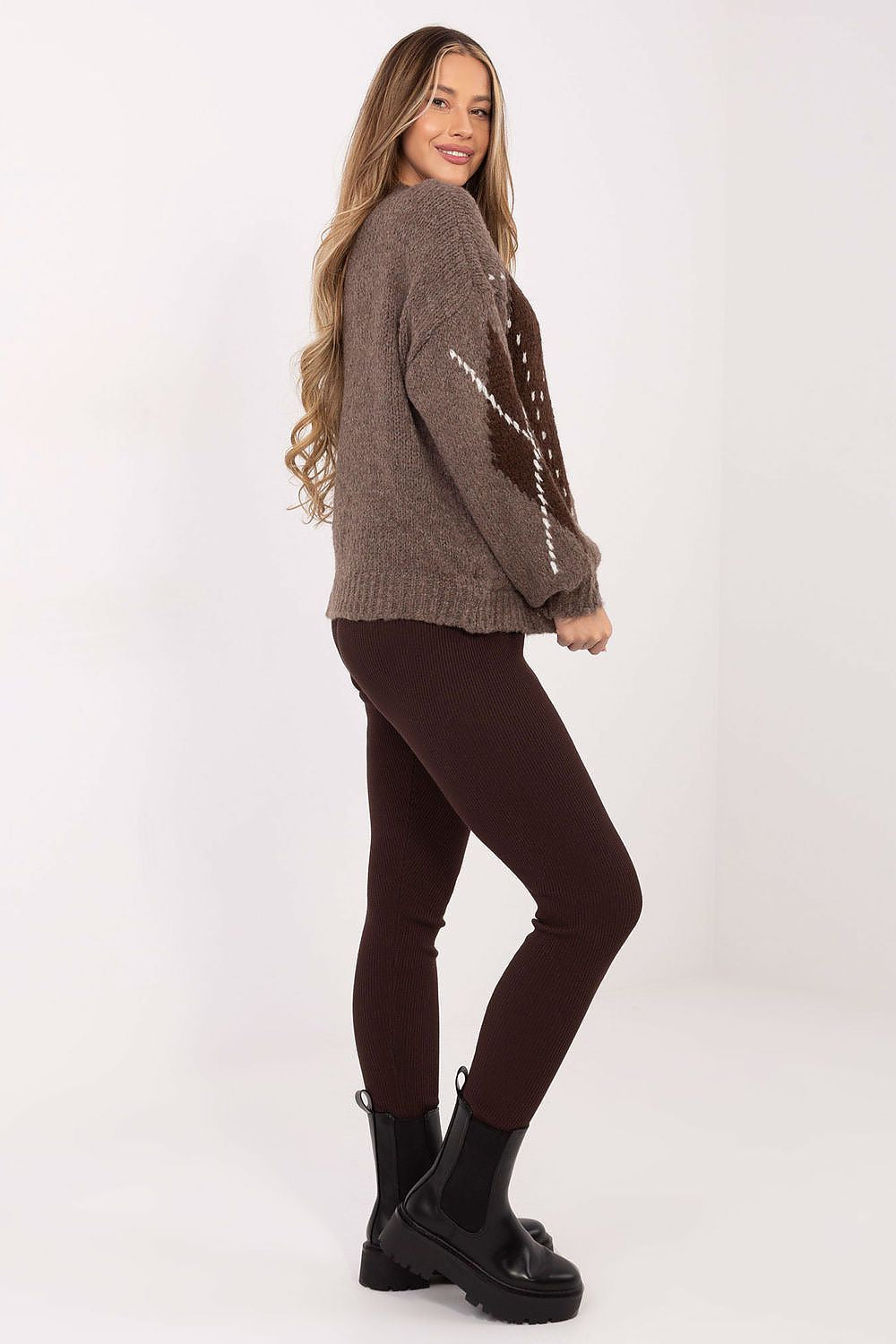 Woman wearing a brown sweater and dark pants on a white background