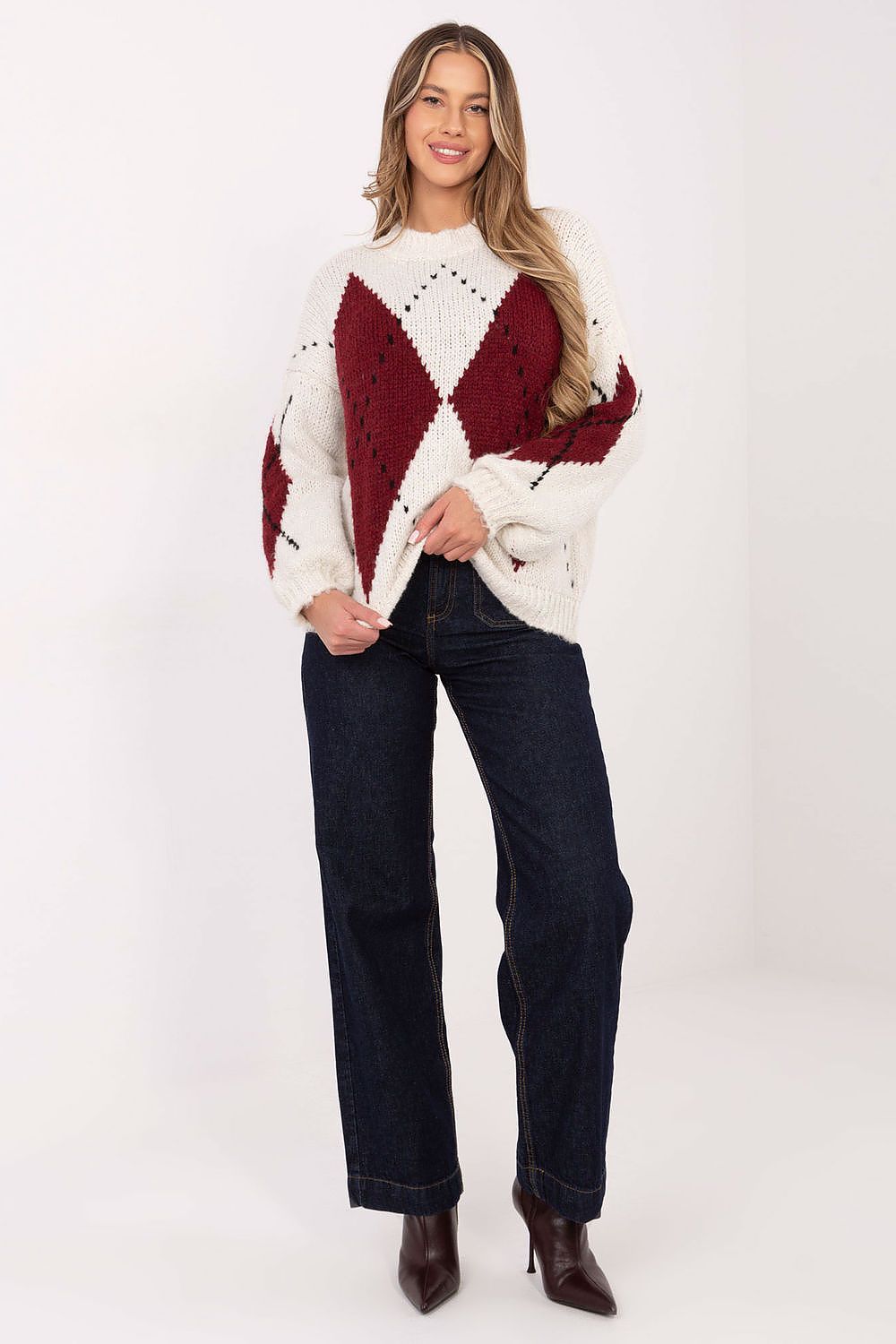 Woman wearing a white and red patterned sweater with dark jeans on a white background