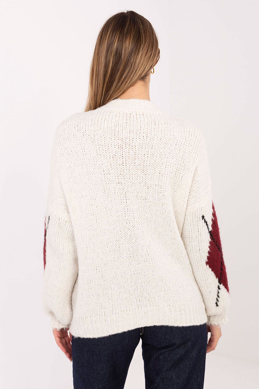 Person wearing a cream sweater with red and black patterned sleeves on a white background