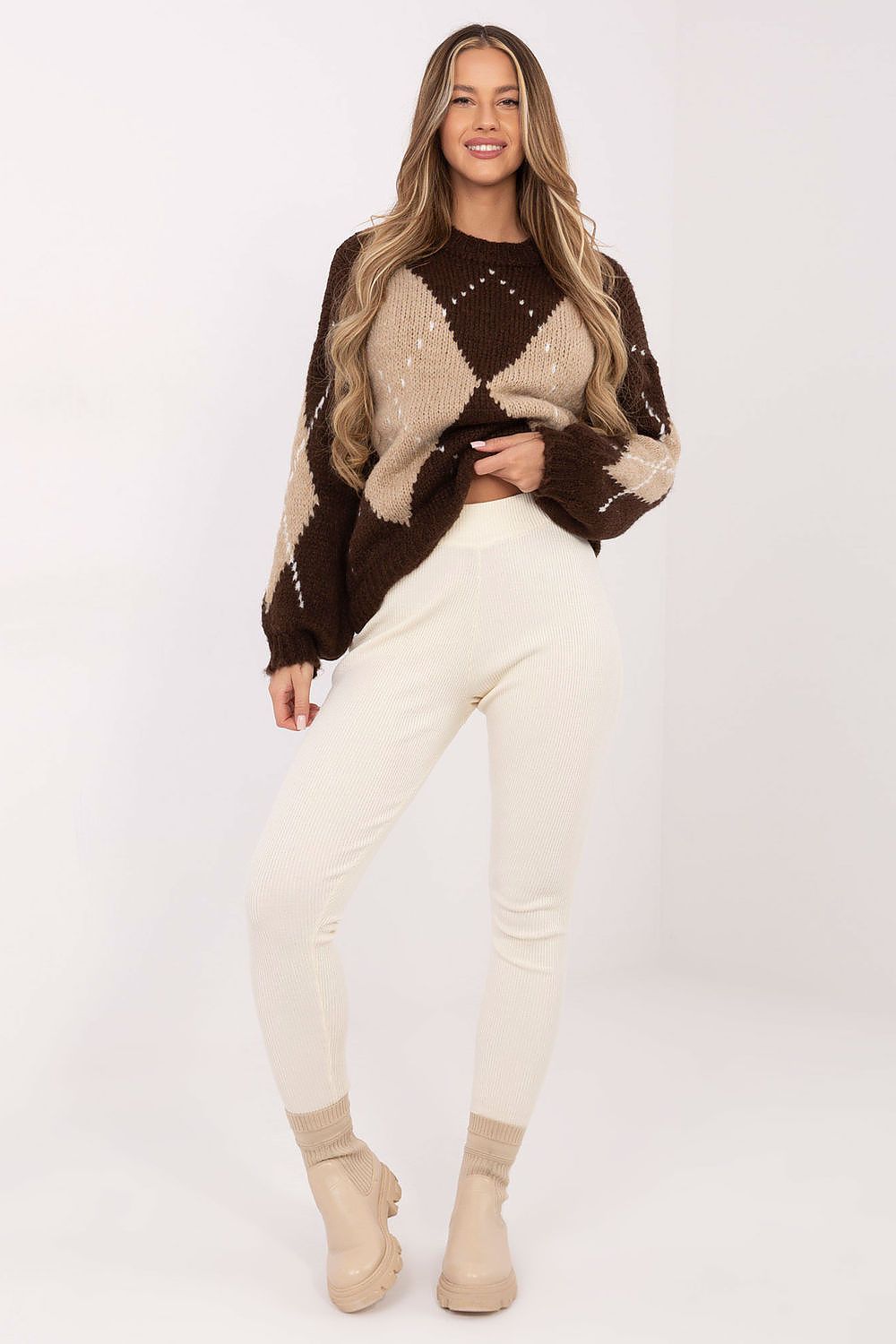Woman wearing a brown and beige patterned sweater with white pants on a white background