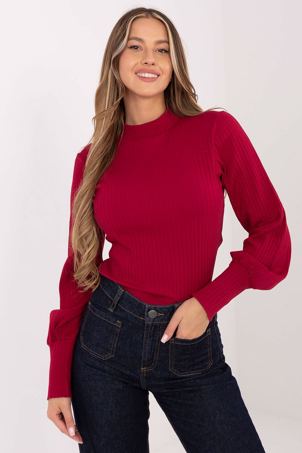 Woman wearing a red sweater and dark jeans on a white background