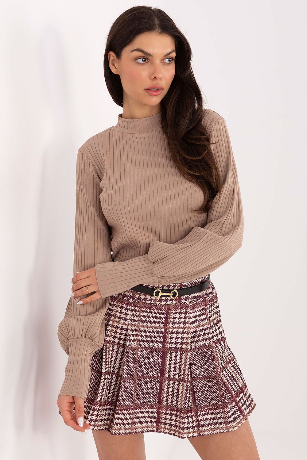 Woman wearing a beige ribbed sweater and plaid skirt on a white background