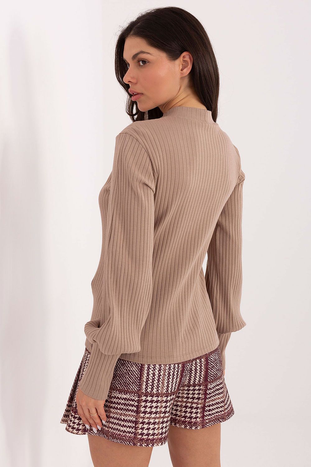 Woman wearing a beige ribbed sweater and patterned shorts on a white background