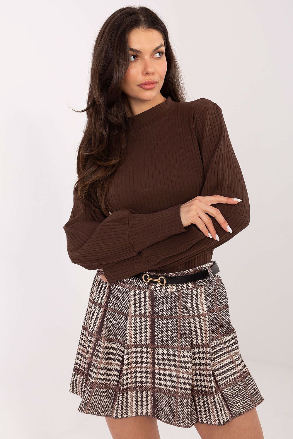 Woman wearing a brown ribbed sweater and plaid skirt on a white background