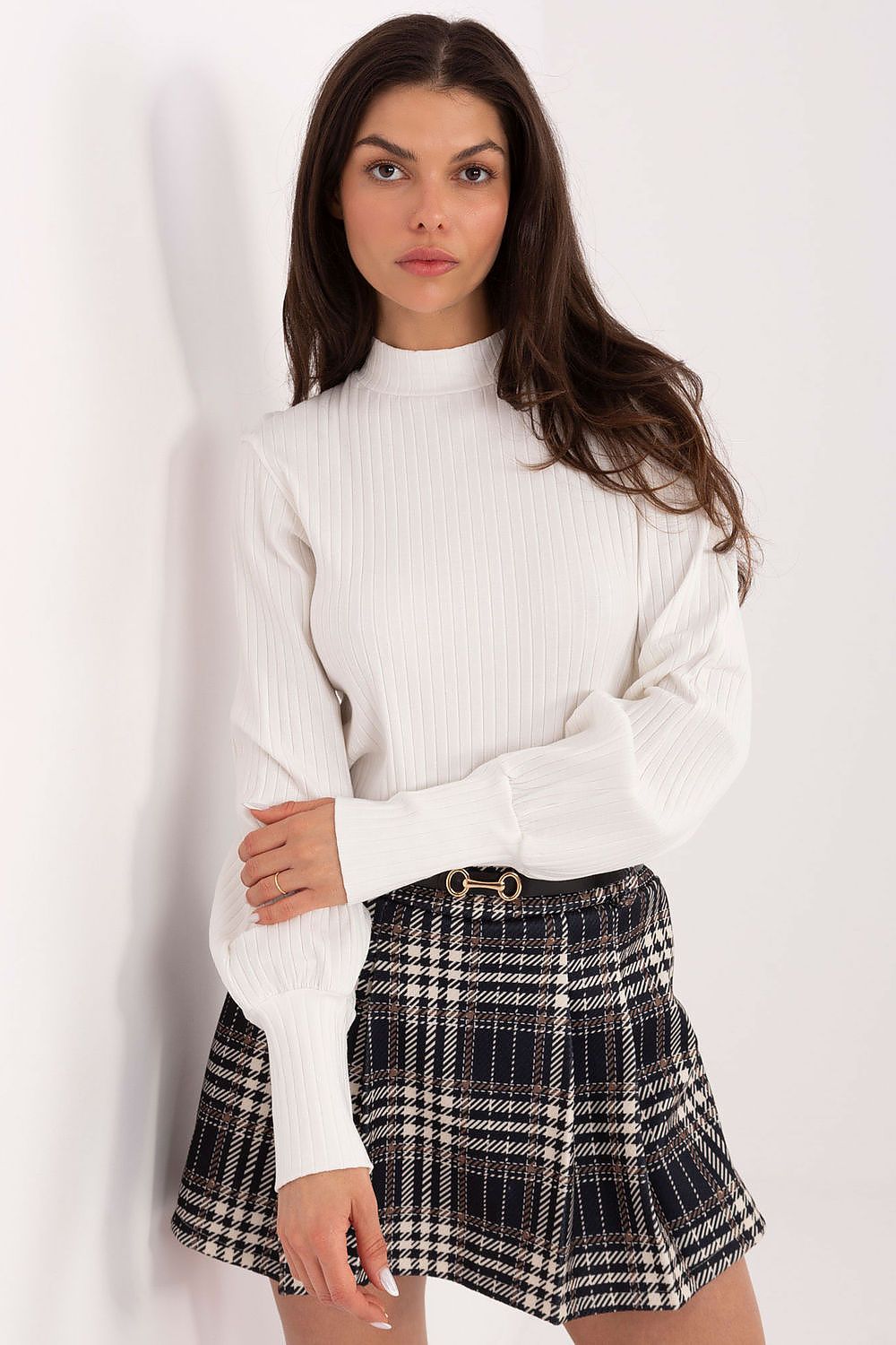 Woman wearing a white ribbed sweater and plaid skirt on a white background