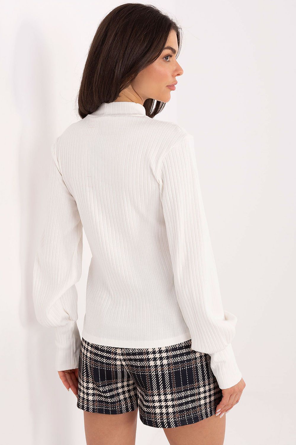 Woman wearing a white blouse and checkered shorts on a plain background