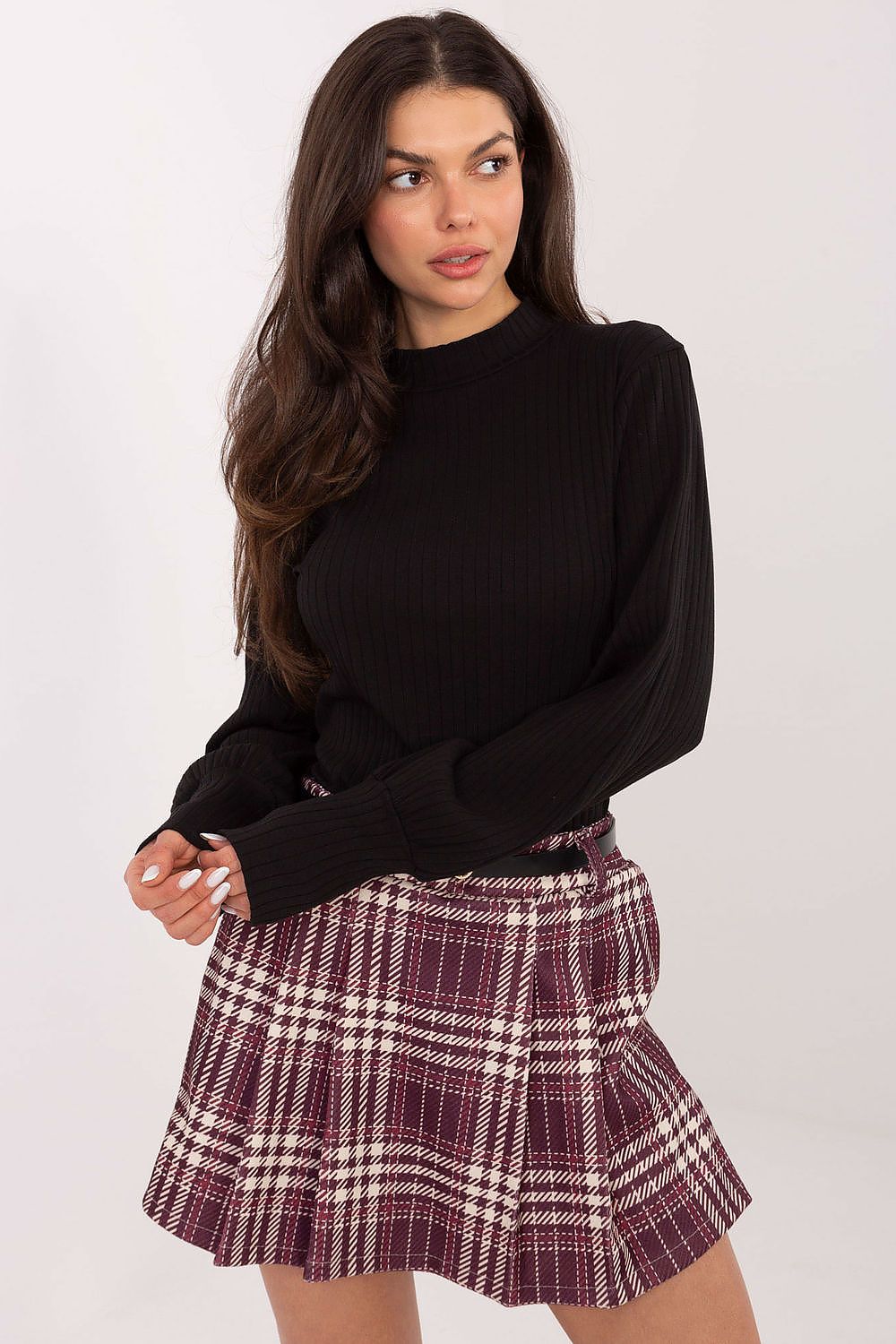 Woman wearing a black long-sleeve top and plaid skirt on a white background