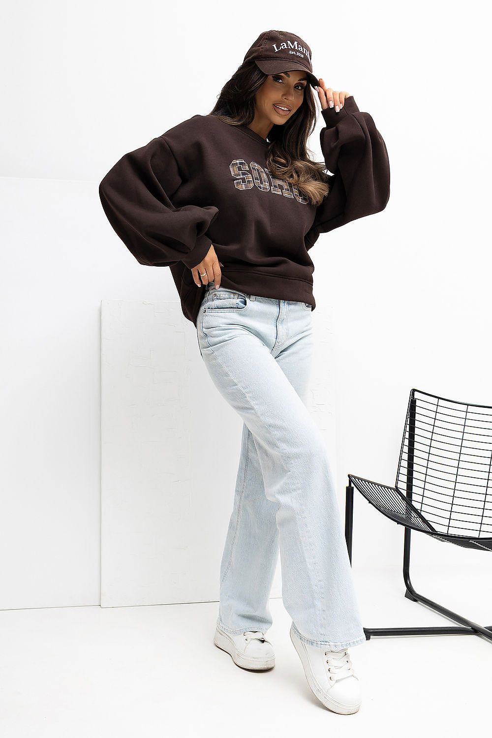Person wearing a brown sweatshirt, light blue jeans, and white sneakers against a white background.