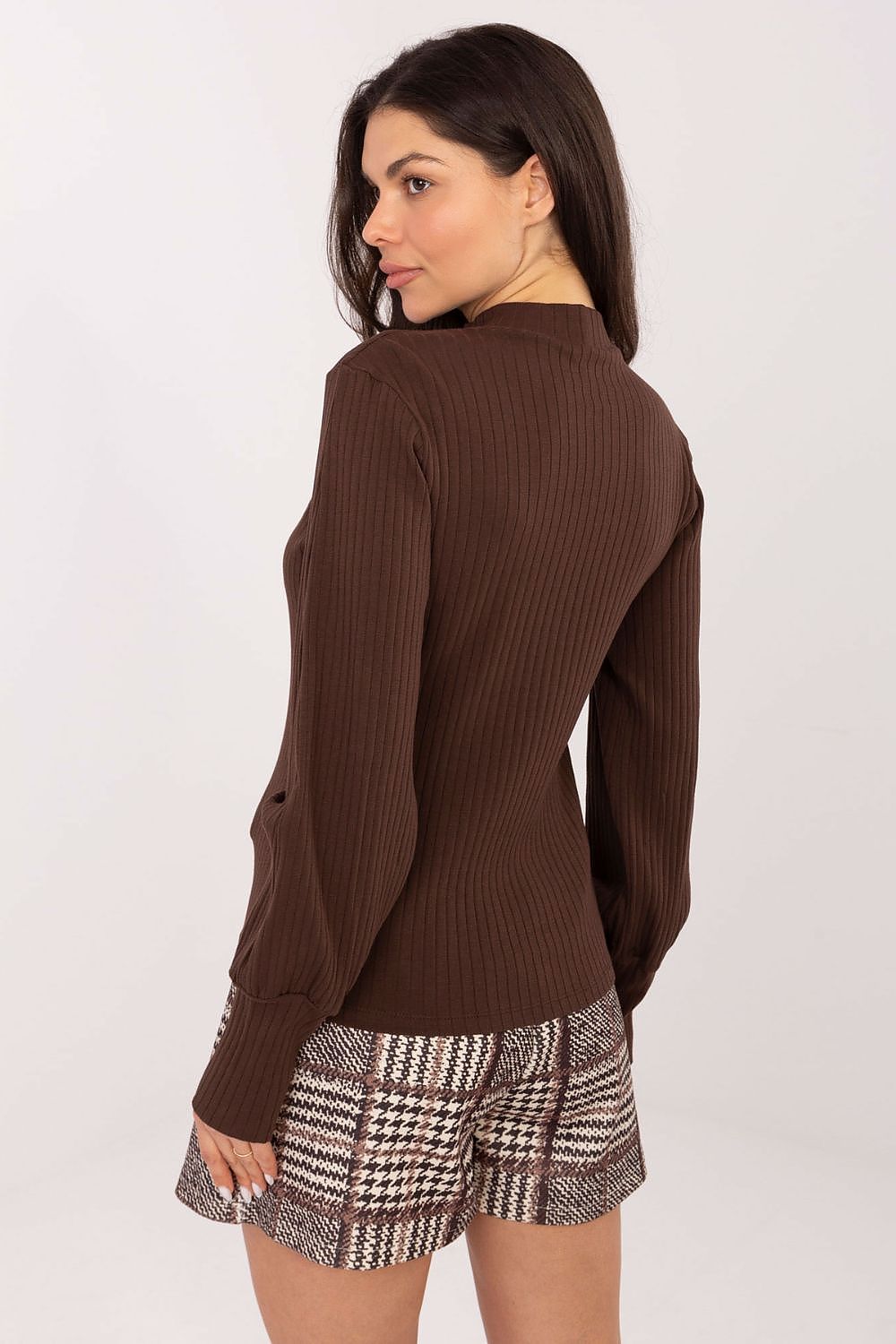 Woman wearing a brown ribbed sweater and patterned shorts on a white background