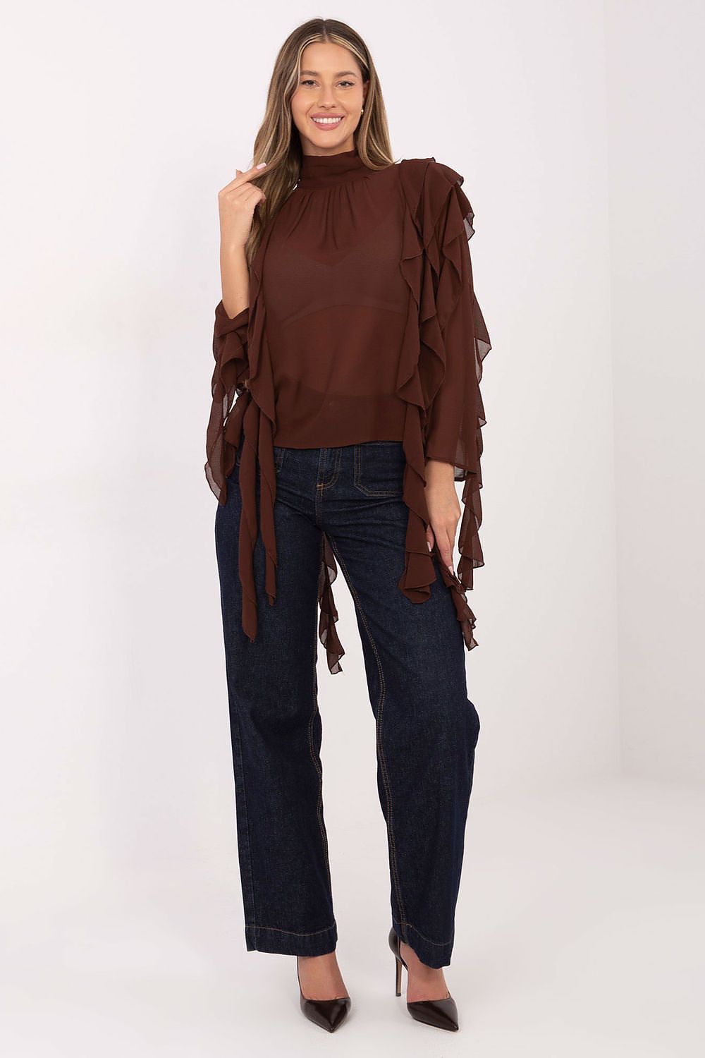 Woman wearing a brown ruffled blouse and dark jeans on a white background