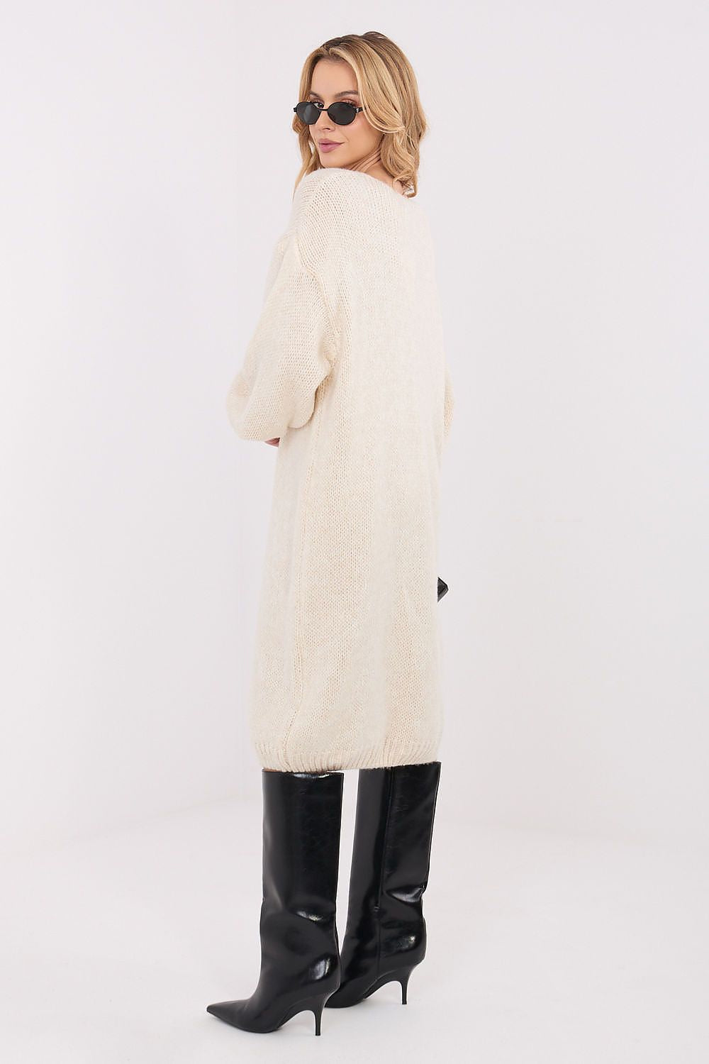 Woman wearing a long cream coat and black knee-high boots on a white background