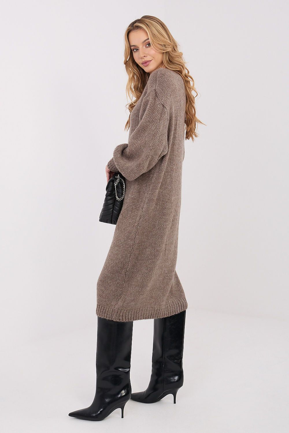 Woman wearing a long brown sweater and black boots on a white background