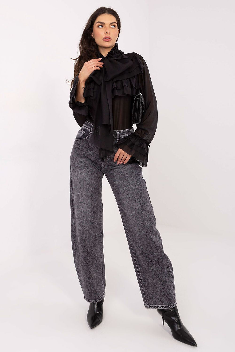 Woman wearing a black ruffled blouse and gray jeans on a white background