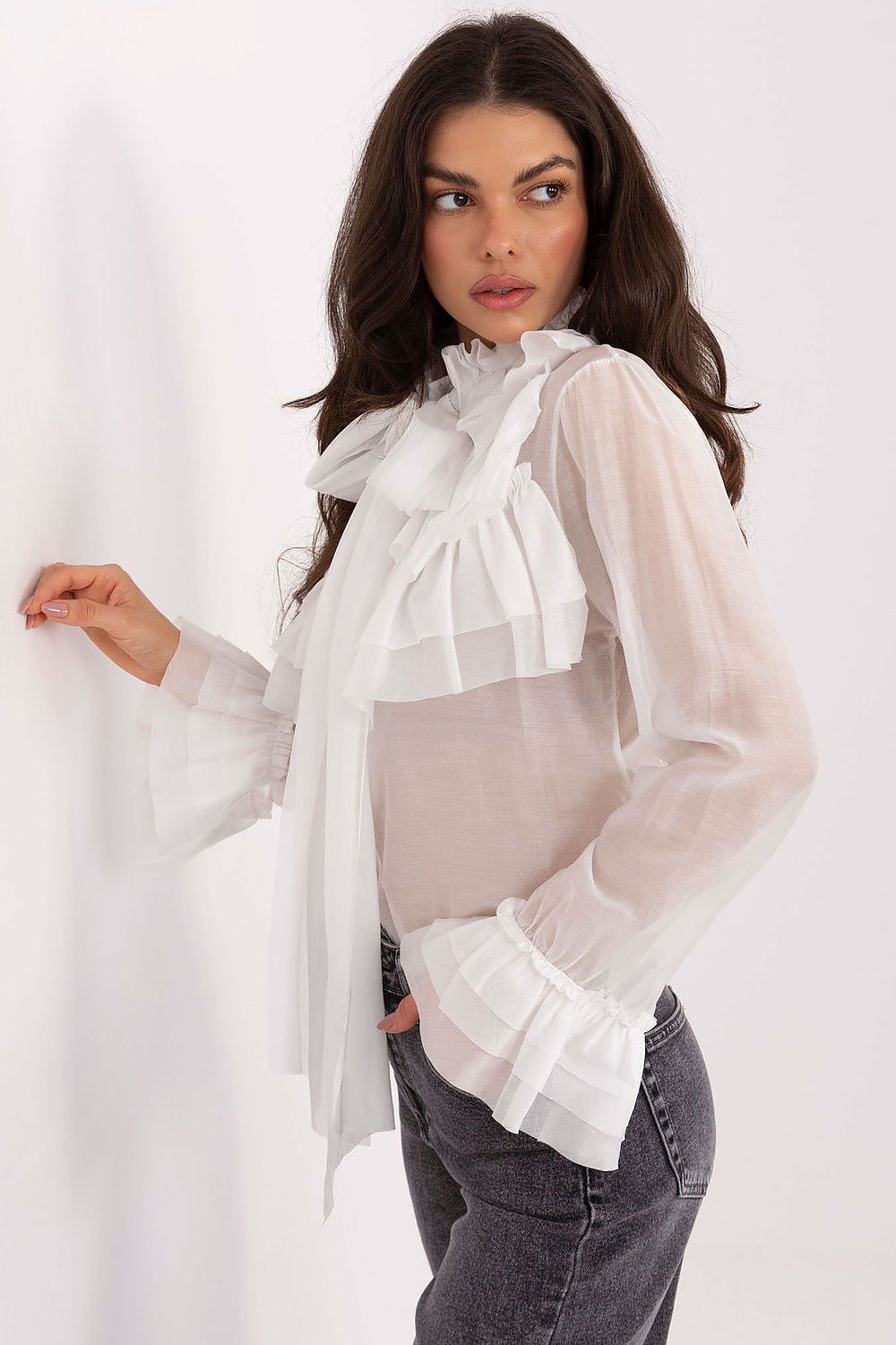 Woman wearing a sheer white blouse with ruffled details on a white background