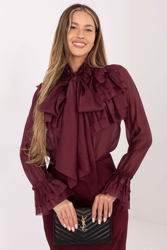 Woman wearing a burgundy blouse with ruffles holding a black handbag against a white background