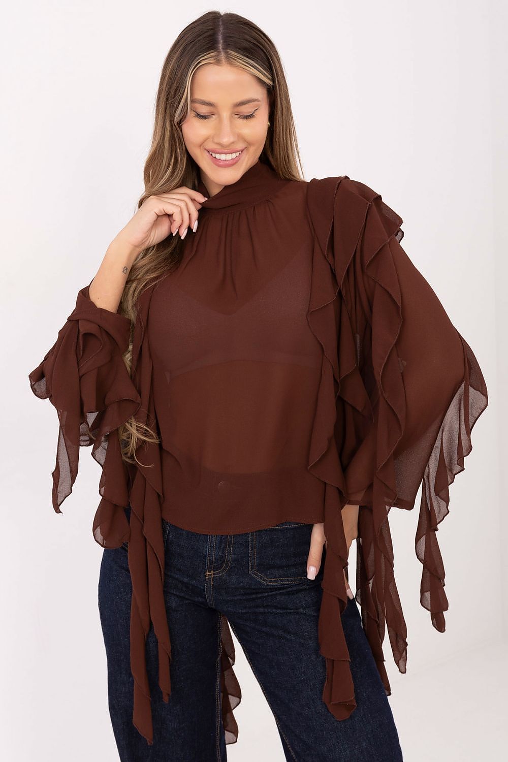 Woman wearing a brown ruffled top and dark jeans on a white background