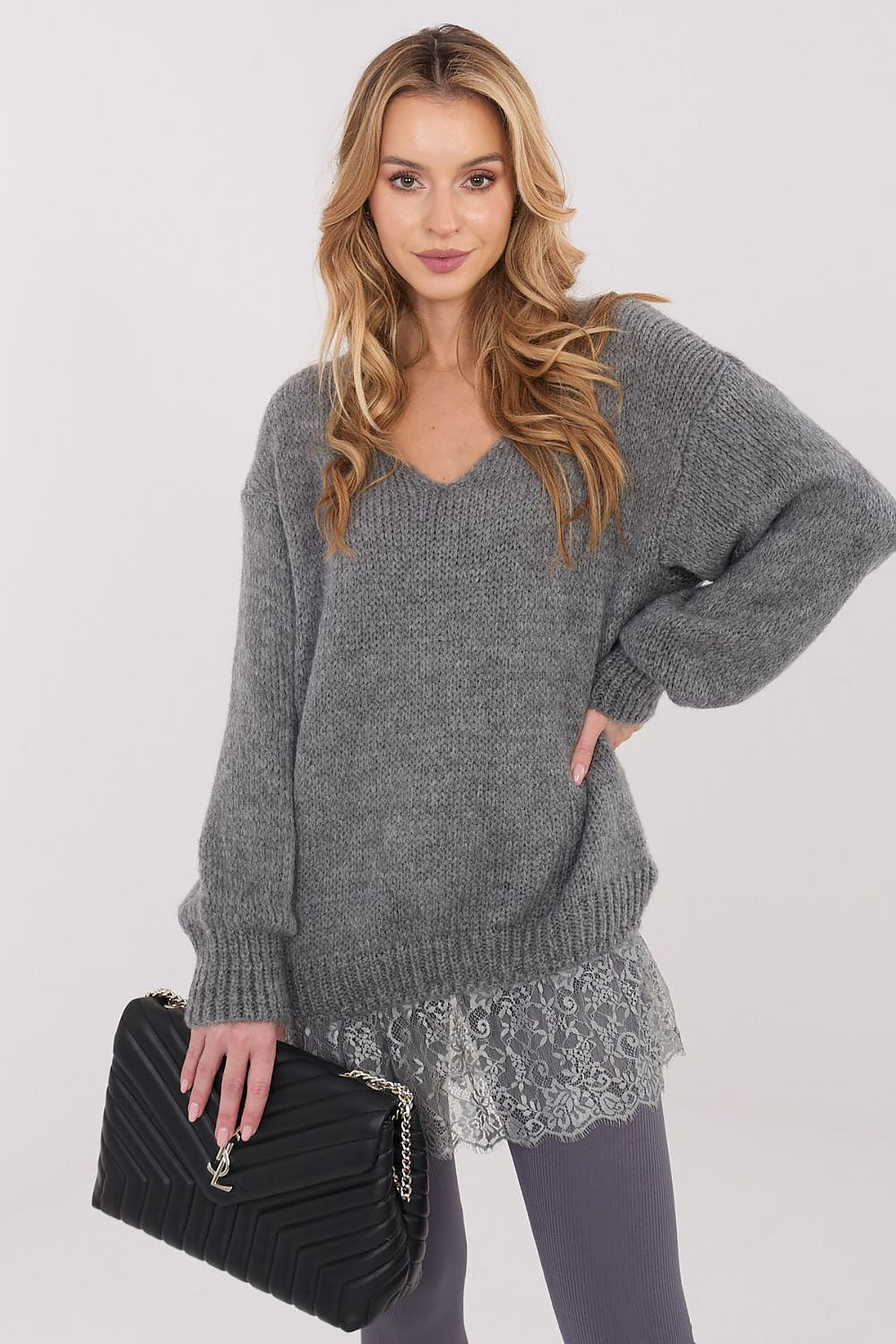 Woman wearing a gray sweater with lace trim holding a black clutch against a white background