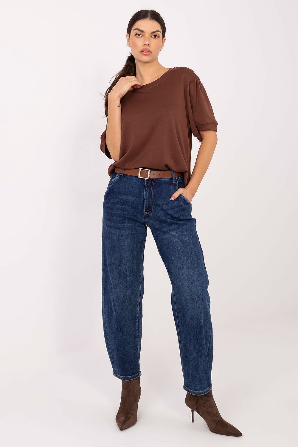 Woman wearing a brown one-shoulder top and blue jeans on a white background