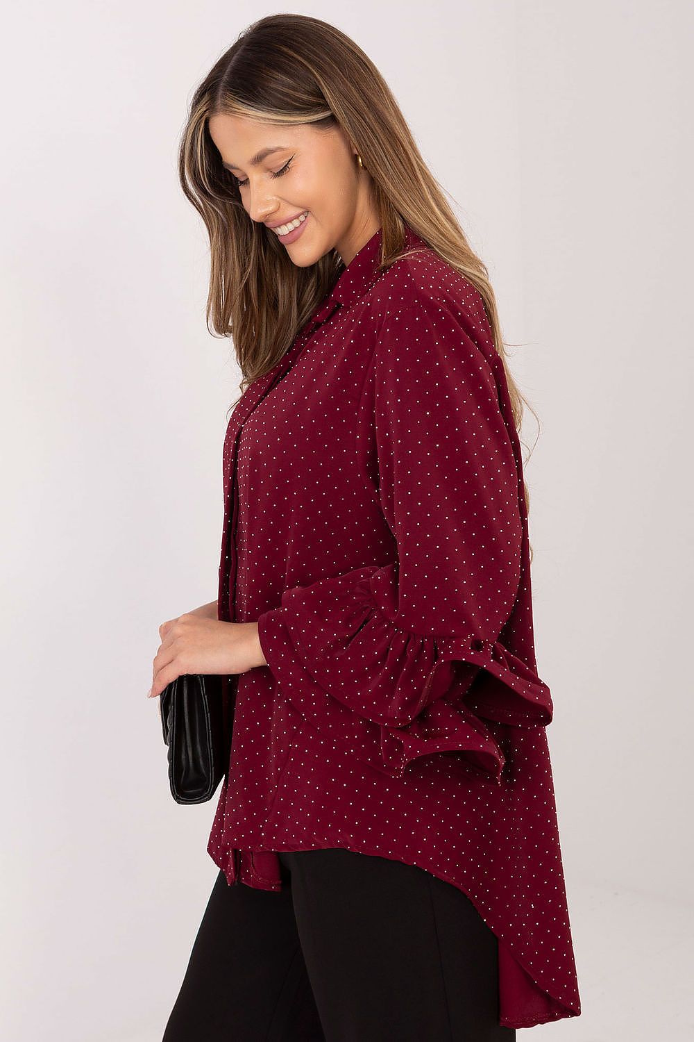 Woman wearing a burgundy polka dot blouse with ruffled sleeves on a white background